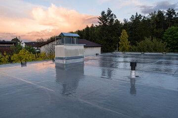 Flat roof covered with bitumen membrane and silver lacquer with chimney on a private house. Reflections after rain - obrazy, fototapety, plakaty