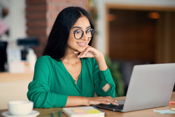 Attractive indian woman studying online at cafe, using laptop