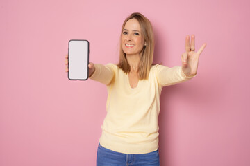 Naklejka premium Young smiling woman showing mobile phone screen with okay sign isolated over pink background.
