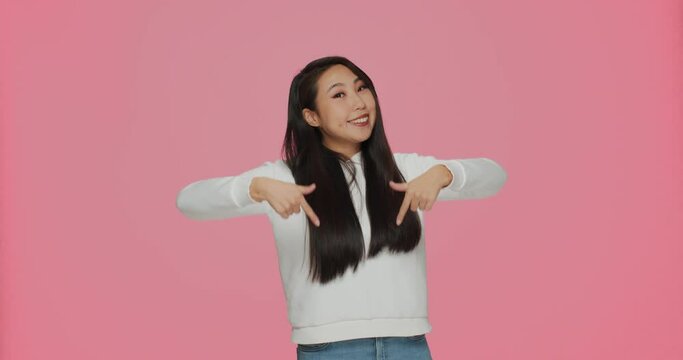 Smiling asian girl point with fingers down at good sale offer look downward recommending service on pink background