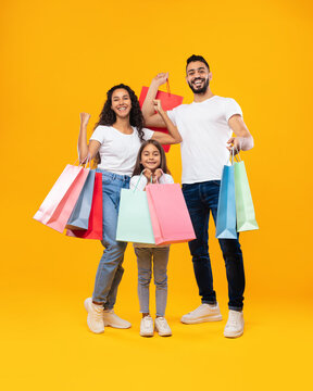 Middle-Eastern Family Holding Shopping Bags Standing On Yellow Studio Background