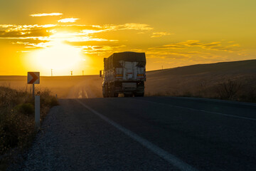Back view of truck drives on a country road and the sunset in background.