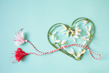 Green and turquoise background with a heart of snowdrops and red and white lace with tassels. Postcard for the holiday on March 1, Martisor, Baba Marta.