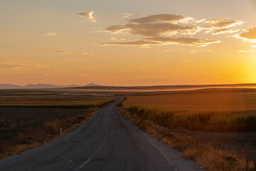 Asphalt road between fields and sunset in the background. Konya, Turkey.