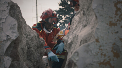 Black rescuer talking with colleague while sitting near rubble and rescuing survivors after disaster