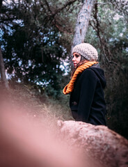Joven mujer con gorro, chaqueta y bufanda, disfrutando de la naturaleza en pleno bosque. 