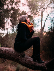 Joven mujer con gorro, chaqueta y bufanda, disfrutando de la naturaleza en pleno bosque. 