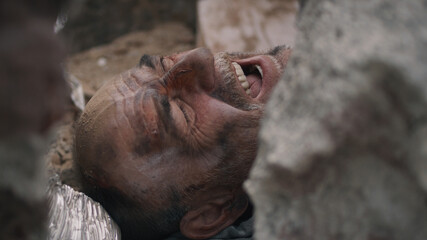 High angle of aged male survivor screaming for help while lying under remains of destroyed building after earthquake