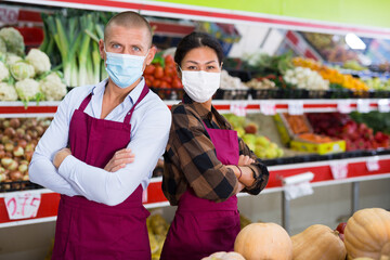 Asian woman and European man in uniform and face mask standing among shelves with fruits and...