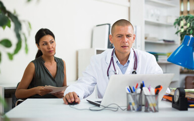 Fototapeta premium Middle aged asian female patient visits young doctor in office at the hospital