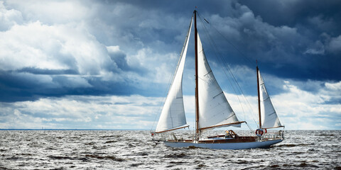 Old expensive vintage wooden sailboat (yawl) close-up, sailing in an open sea. Dramatic cloudscape. Coast of Maine, US