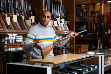 Fototapeta premium Handsome positive adult male in hunting shop with rare collectible rifle in hands