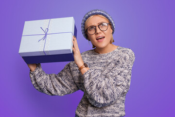 Close-up portrait of a woman shake curious gift box looking up isolated over purple color background. New year.