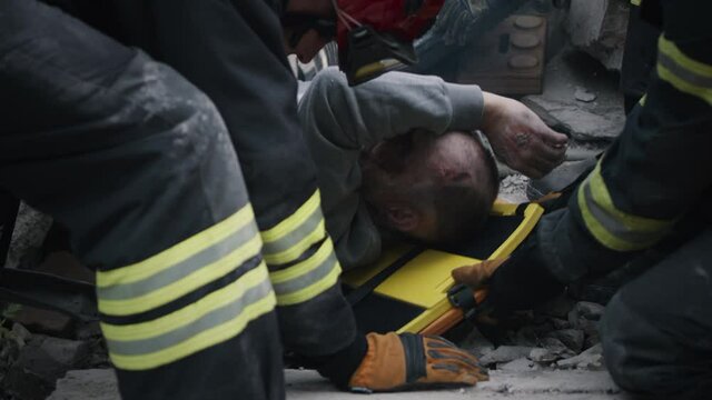 Crop emergency service workers using spinal board to save injured aged survivor from ruins after cataclysm