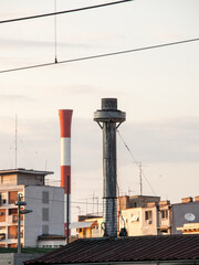 individual metal chinmey in the center of belgrade, serbia, with a blurred industrial red and white chimney in background, taken during a sunny afternoon, used for industry and energy production