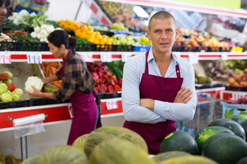 Portrait of confident salesman of fruit and vegetable store standing near counters..