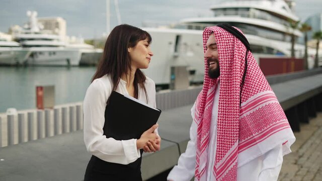 Smiling saudi businessman speaking with female professional yacht broker before buying boat in port