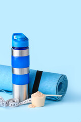 Scoop with protein powder, measuring tape, bottle and fitness mat on color background