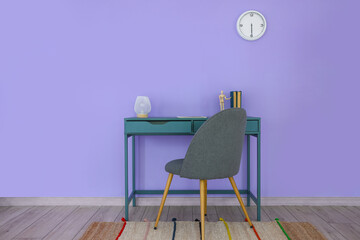 Table with lamp, books and mannequin doll near color wall