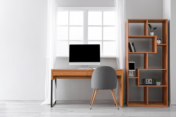 Wooden table with computer and shelving unit near window in office