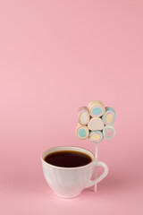 Black coffee in a white cup and a set of marshmallows on a stick on a pink background. The concept of a fun breakfast. Place for text.