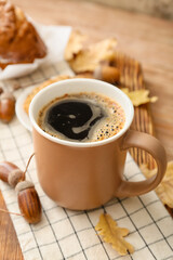 Cup of coffee with acorns and autumn leaves on table, closeup