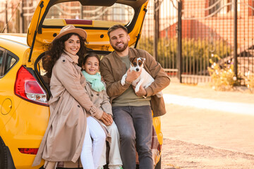 Happy parents with little daughter and cute dog sitting in car trunk outdoors