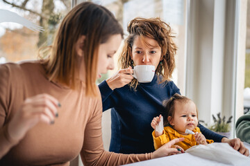 Woman hold child two female friends sitting at cafe or restaurant by the table holding small caucasian baby having a cup of coffee real people friendship leisure concept in bright day selective focus