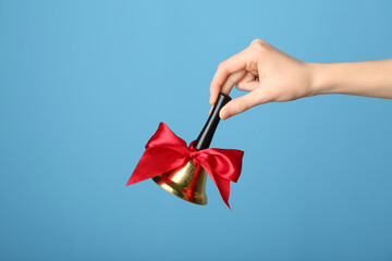 Woman holding golden Christmas bell on blue background, closeup