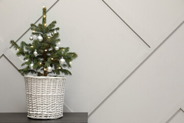 Fototapeta premium Beautiful decorated Christmas tree in pot on table near light wall