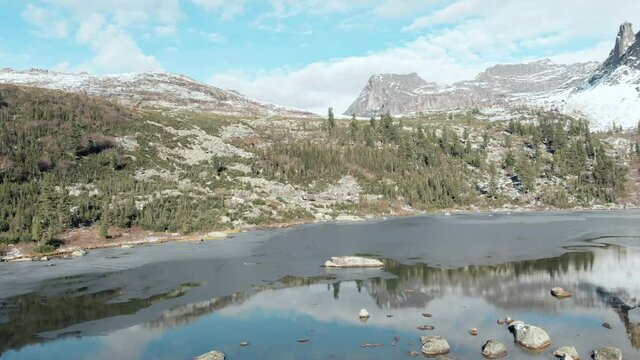 Aerial view of the rocks of the Sleeping Sayan behind Lake Raduzhnoe. There is snow, the sky is blue, stones and cold water. Ergaki park