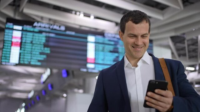 Tourist traveler man using mobile phone of flight plane arrivals board timetable in airport terminal for trip travel. Businessman typing text message on smartphon for check-in, Technologies business