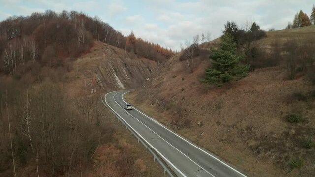 An aerial drone view of car driving fast on a winding road running through a canyon in late autumn. The drone is moving upwards.