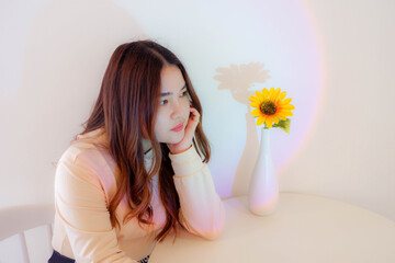 A young woman sitting alone with a background of flowers and lights.