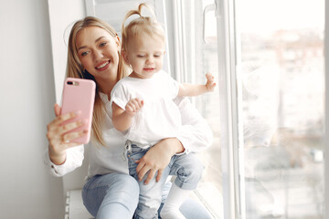 Mother and little daughter spend time together sitting on the windowsill.