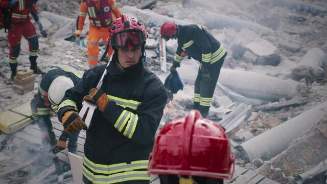 Male emergency workers in uniform talking with each other while working on remains of demolished building after earthquake