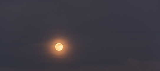 Rising full moon and light clouds against the backdrop of a twilight sky