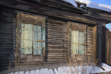 Detail of the facade of an old wooden rural house in traditional Russian style. Windows with carved frames and closed shutters. Metal bolts and hooks. Winter, blue sky. Village Byngi, Ural, Russia