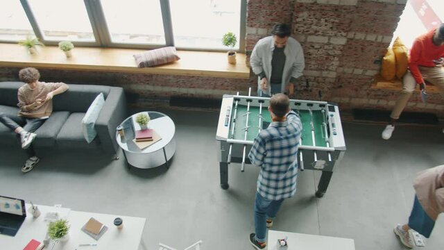 Happy young people are relaxing during work break playing ping pong and foosball in office. Modern youth lifestyle and positive emotions at work concept.