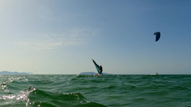 Low angle pov of man trying to find balance on kiteboard and wingfoil on sea surface. Slow-motion sea-level view