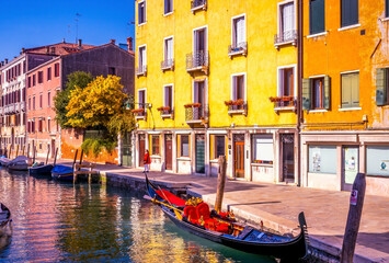 Colorful small canal boats and gondola create beautiful reflection in Venice, Italy.