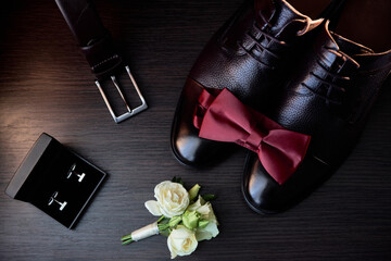 Close up of male shoes, bowtie, belt and  boutonniere on wood background, copy space. Modern man accessories. Wedding details. Top view, flat lay