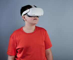 A young guy with Viar glasses. A teenager in a red T-shirt is playing with white virtual reality glasses, looking at something upstairs with interest