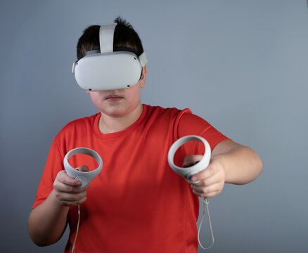 A young guy in viar glasses. A teenager in a red T-shirt plays with white virtual reality glasses, uses joysticks and gamepads