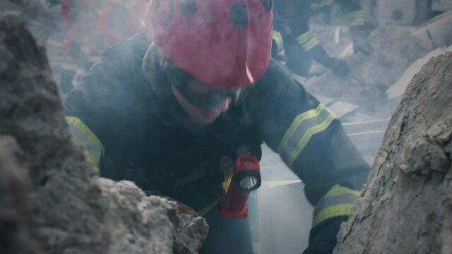 Tracking shot of man in hardhat and goggles speaking to survivors buried under ruins of demolished building after earthquake