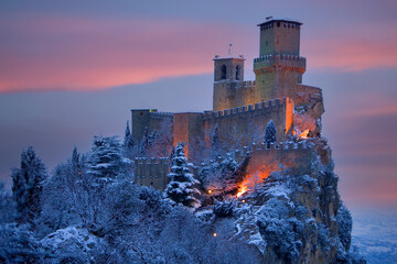 Europe, San Marino. Mountain castle lit at twilight in winter.