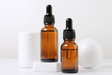 A mock-up of an empty glass dropper bottle made of brown glass stands on a white podium and a white background. Skin care serum, banner or template. The concept of a natural cosmetic product.Copyspace