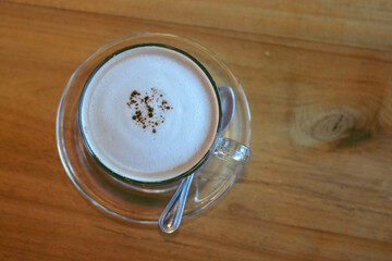 Top view a cup of hot cocoa with milk foam and teaspoon beside put on wooden table background.