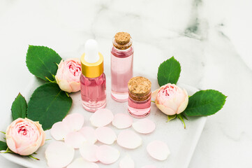 bottles of essential, cosmetic rose oil on a ceramic tray with rose petals and buds. the concept of skin care, beauty, well-being.