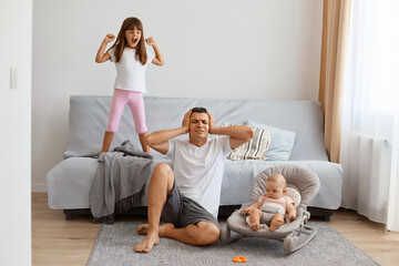Portrait of tired exhausted handsome brunette father playing with his daughters while sitting on...